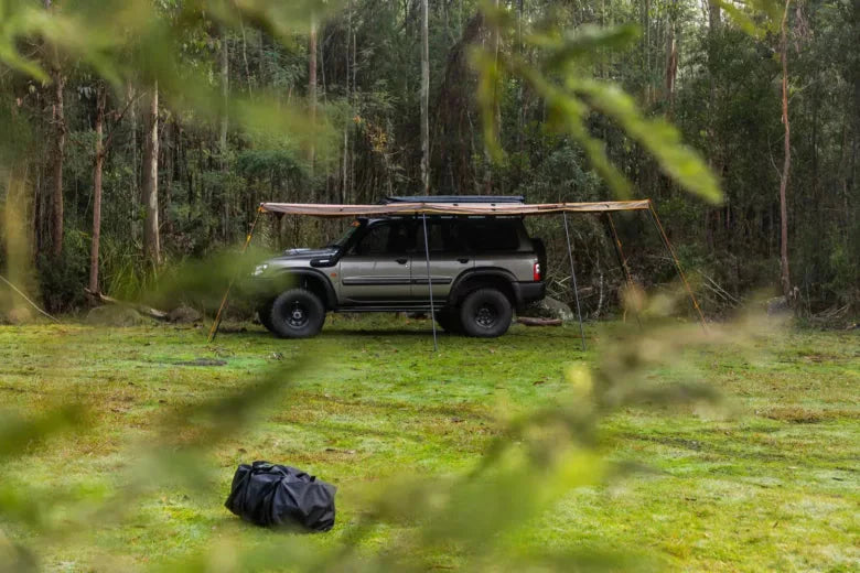 SUV with awning in a field surrounded by forest 
