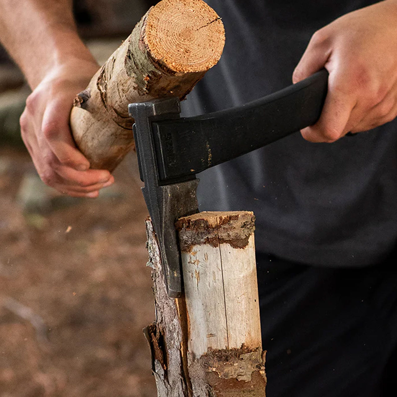 A man firmly grips the Agawa ADK26 Transforming Camp Hatchet and Forest Axe in his left hand while using a piece of wood in his right hand to strike the back of the axe. The blade slices through a log, showcasing the axe's strength and precision in an outdoor setting.