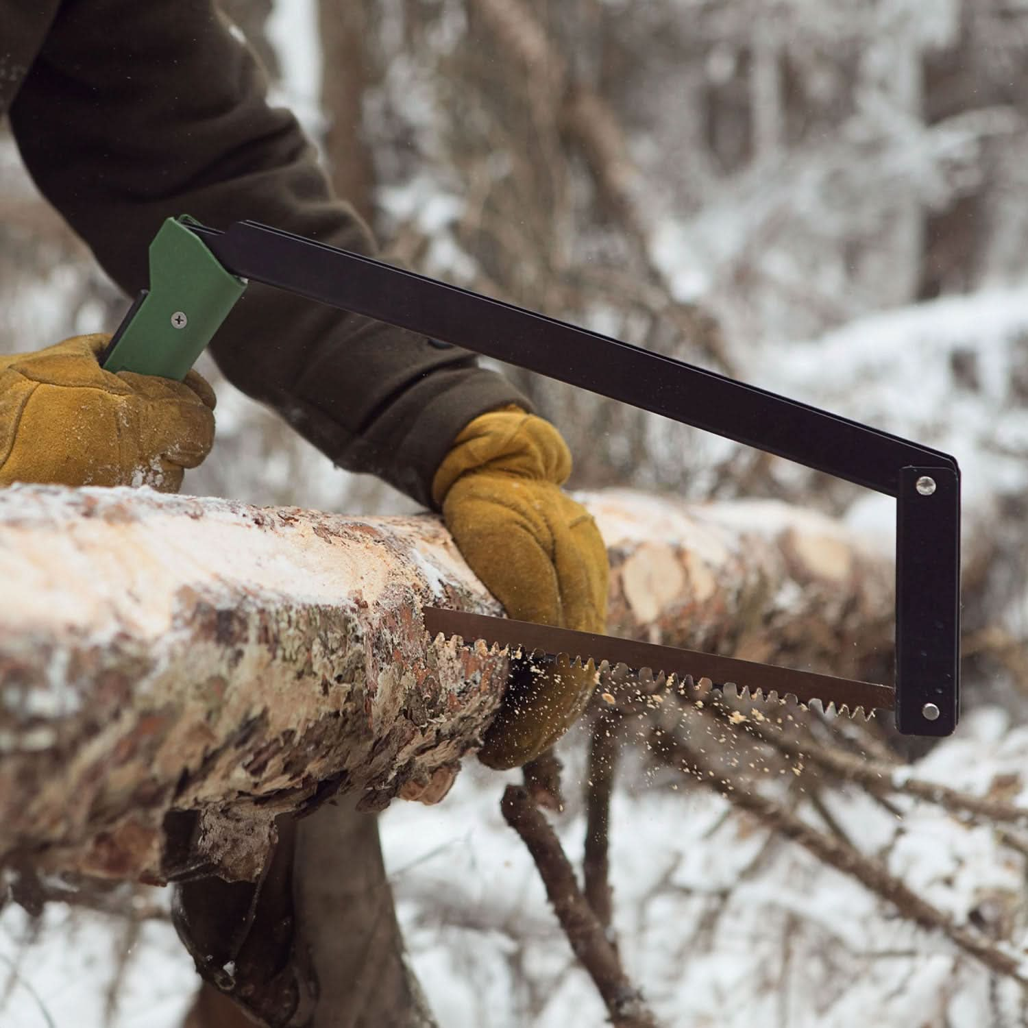 Person wearing leather gloves using the Boreal saw to cut through a felled tree in a snowy winter landscape.