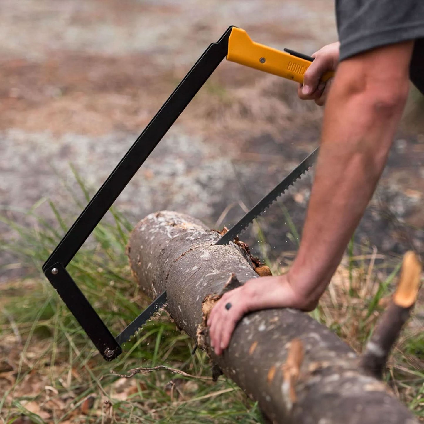 Man using a yellow-handled Boreal saw to cut through a log in an outdoor setting, with the focus on the saw and the log.





