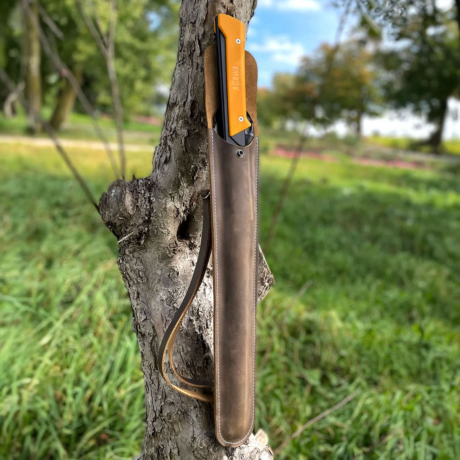 Open Agawa Crazy Horse sheath in dark brown leather, propped against a tree with the yellow-handled Agawa saw visible. The leather carry strap is shown, with an outdoor background in view.