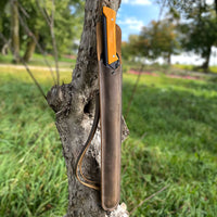 Thumbnail for Open Agawa Crazy Horse sheath in dark brown leather, propped against a tree with the yellow-handled Agawa saw visible. The leather carry strap is shown, with an outdoor background in view.