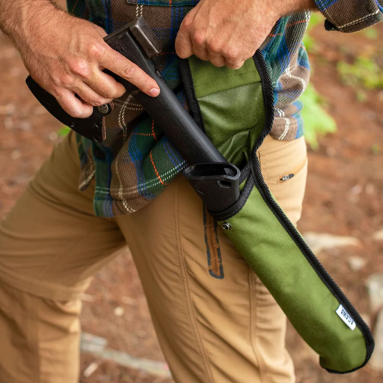 A man with the Agawa ADK26 Transforming Camp Hatchet sheath on his left hip, reaching with his right hand to pull the protected axe blade from the sheath. His left hand holds the sheath open, revealing the bottom half of the axe still resting inside.






